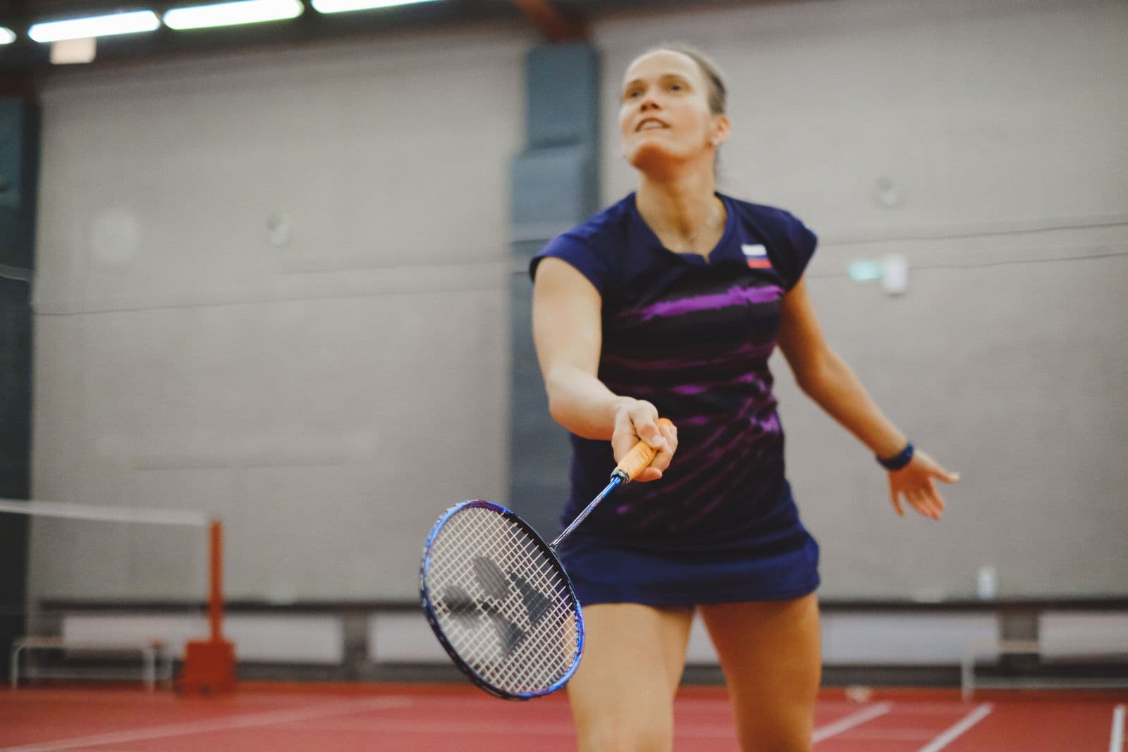 Badminton player in a deep ready position on an indoor court