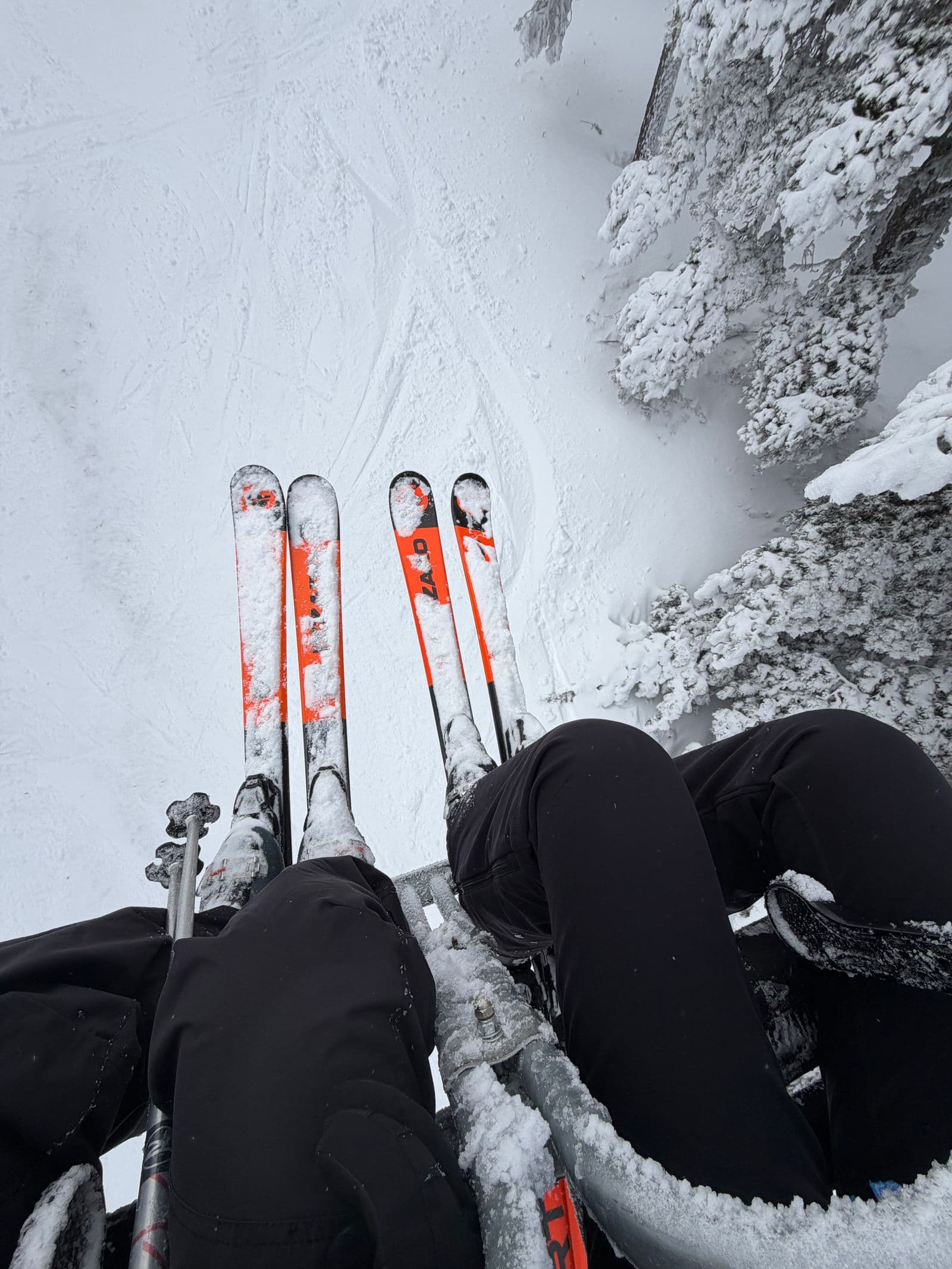 Skiers riding a chairlift over a snowy alpine forest