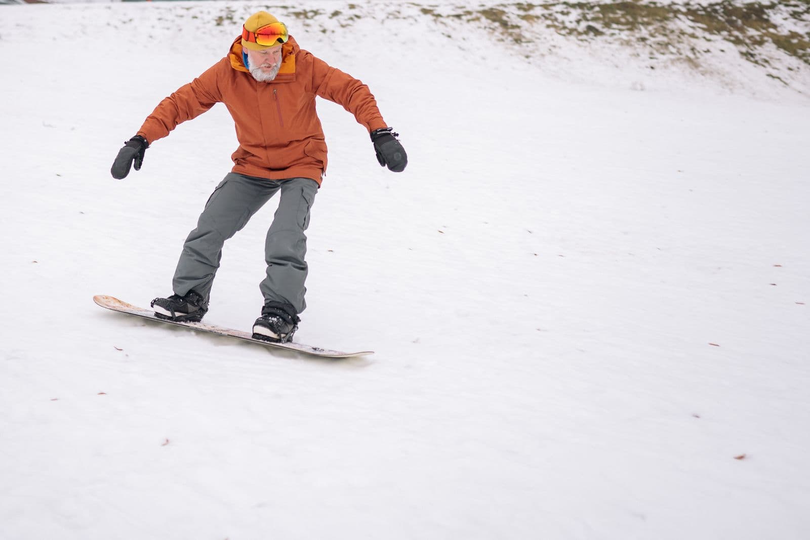 Older snowboarder riding a gentle snowy slope