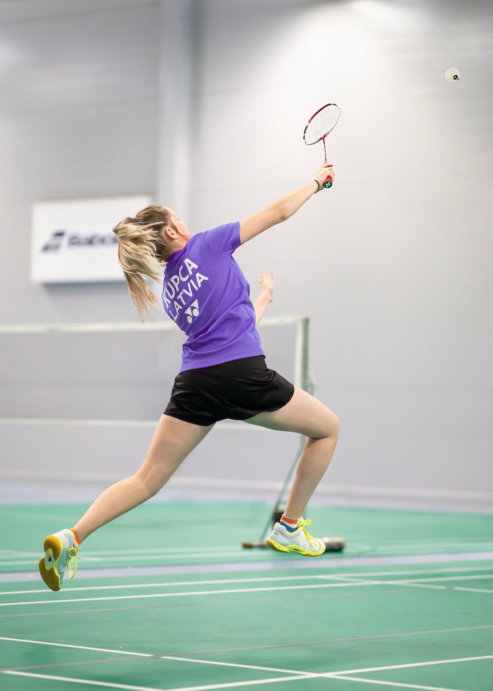Badminton player reaching overhead mid jump smash