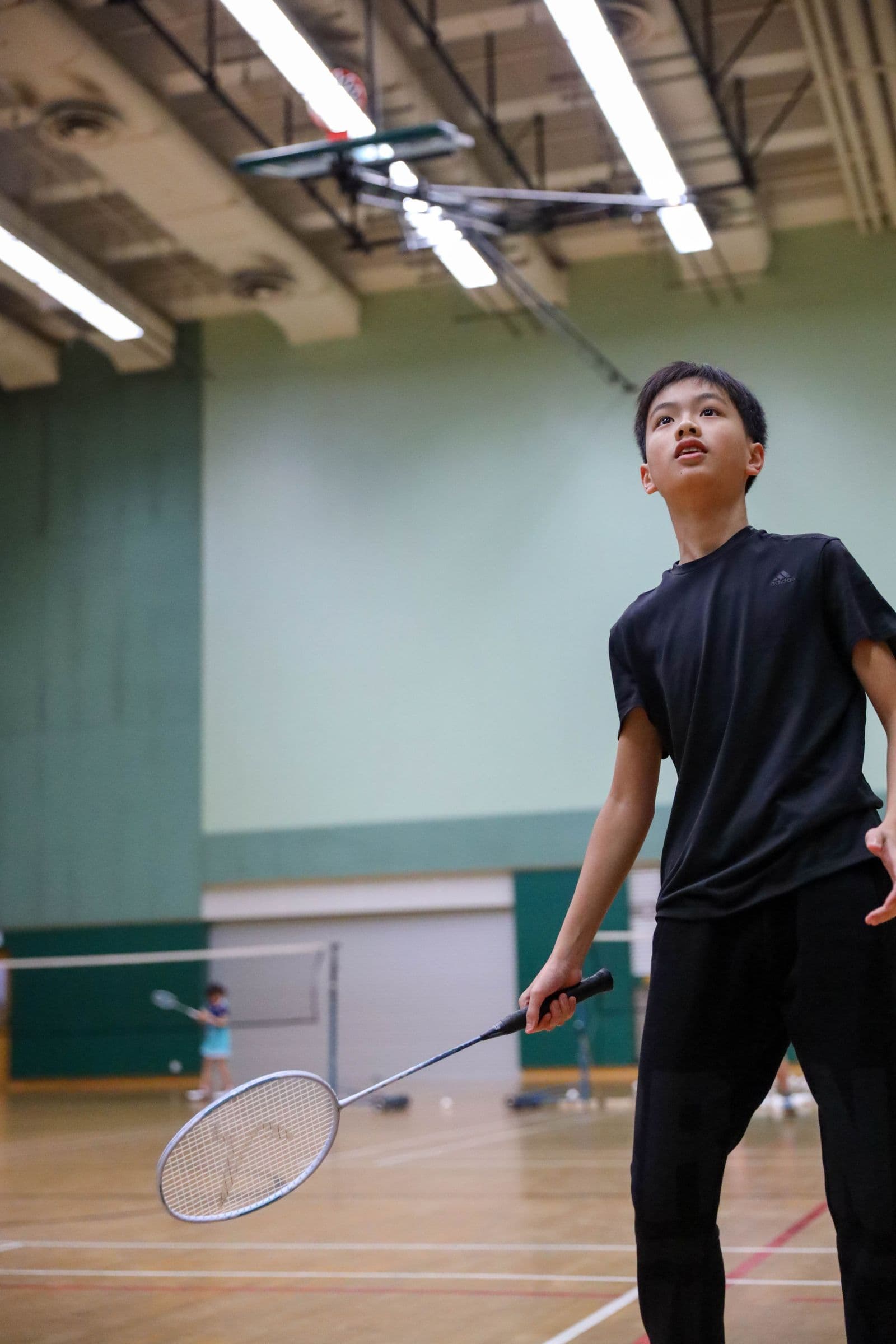 Young player mid-rally in an indoor badminton gym