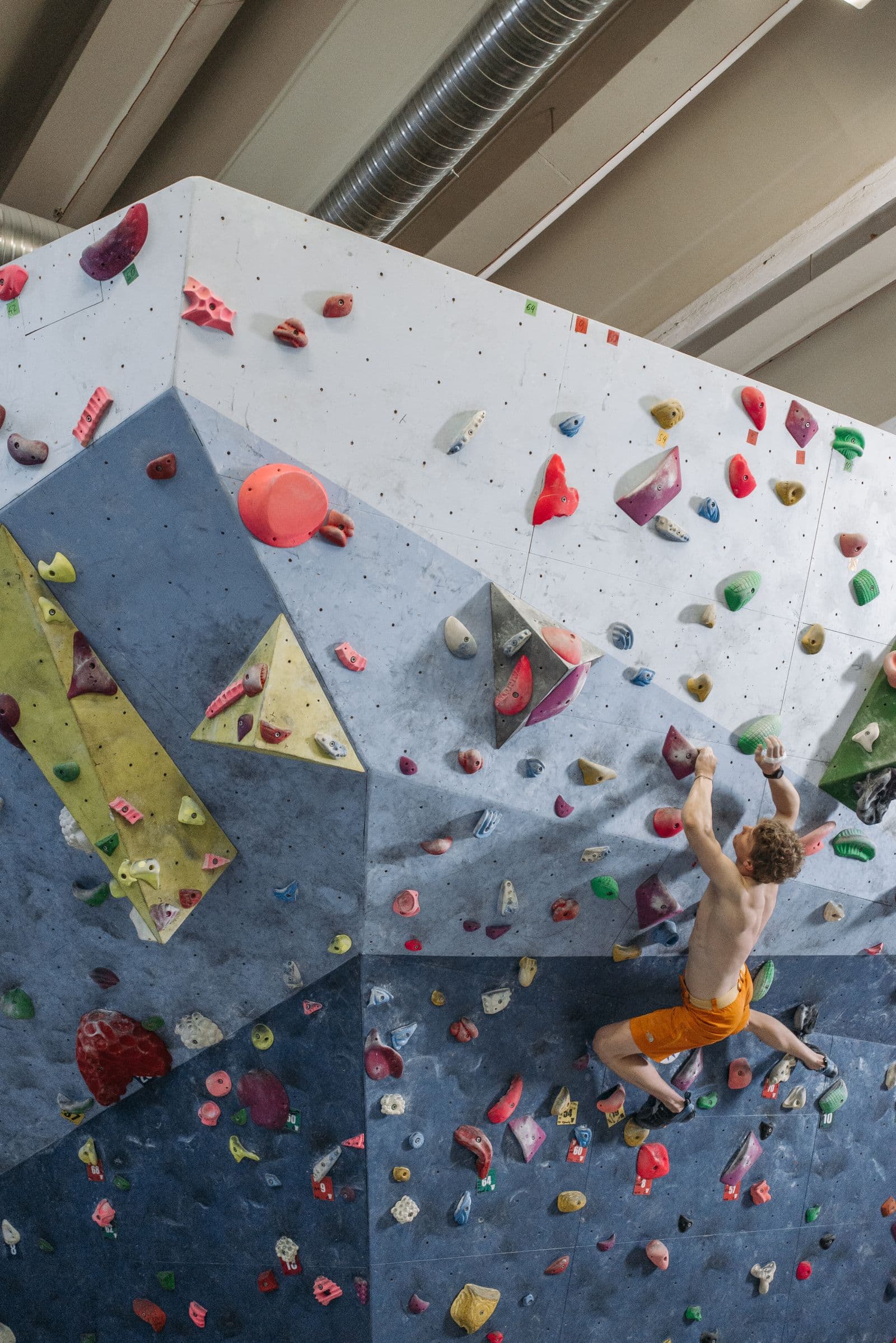 Boulderer on a colorful indoor wall above the mats