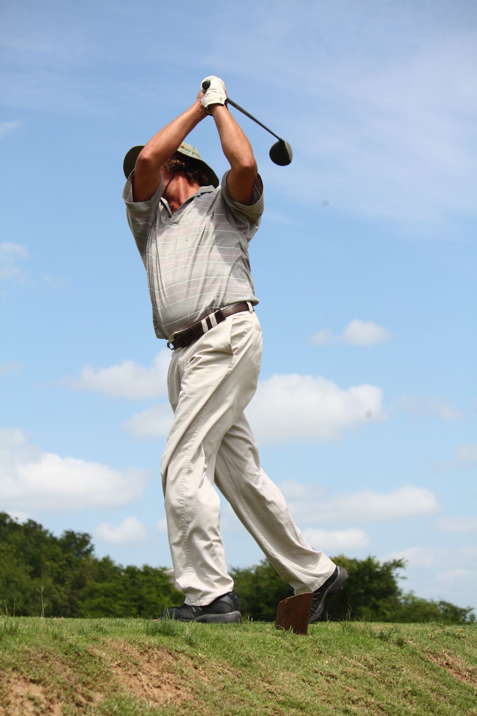 Golfer in mid-swing on a green course under a blue sky