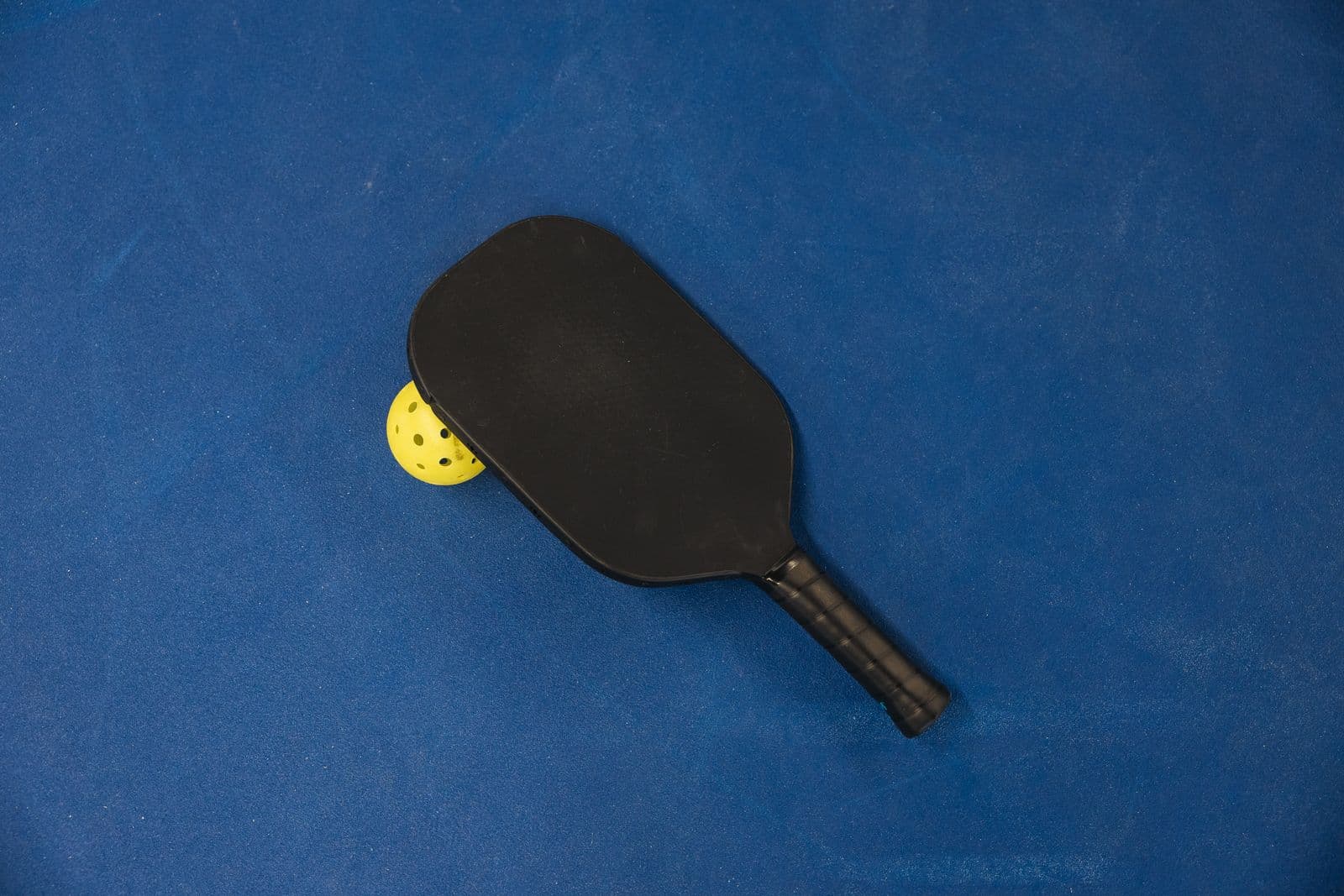 Pickleball paddle and ball on a blue court