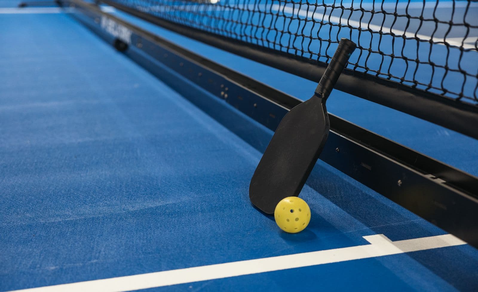 Pickleball paddle and ball resting at the net on a blue court