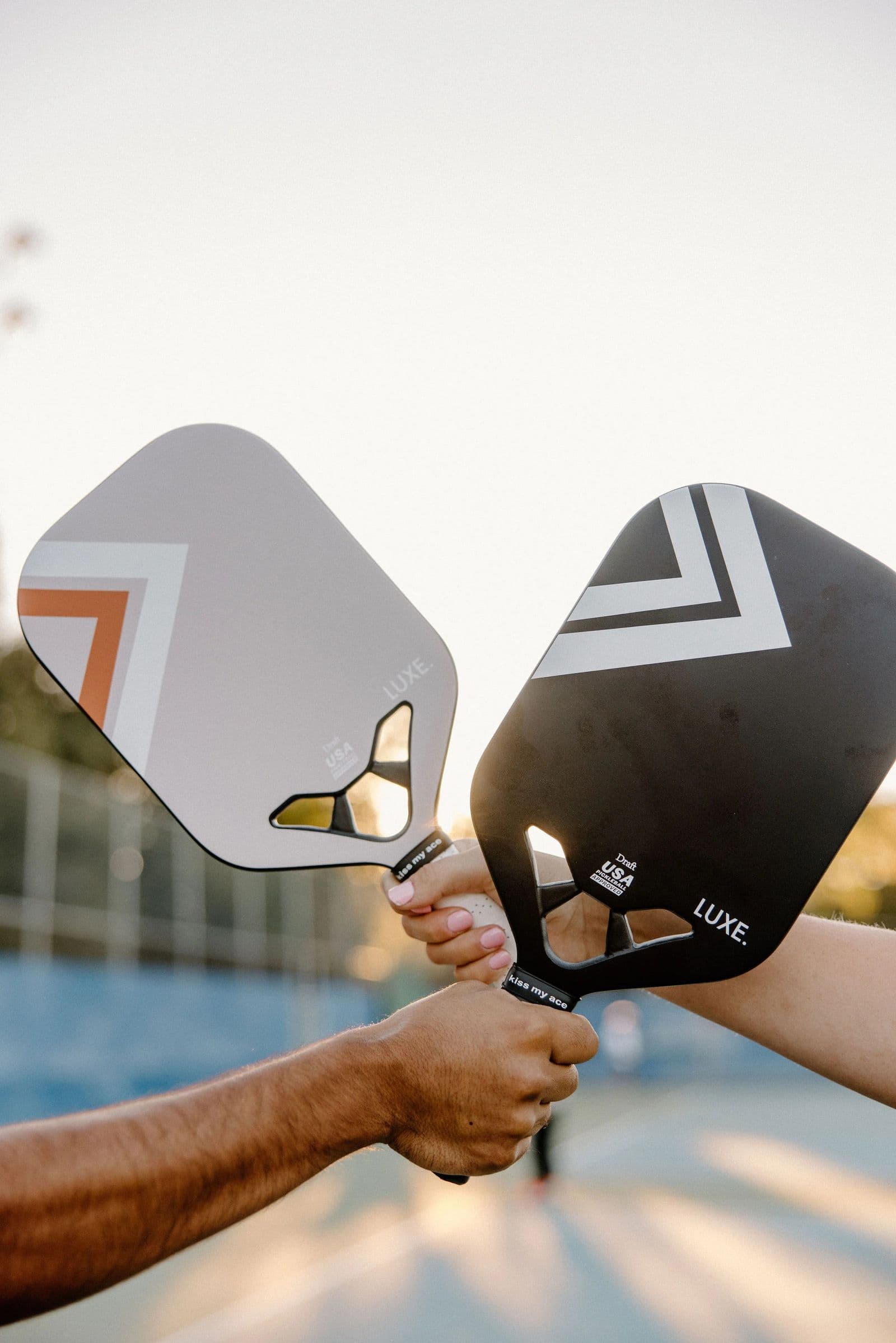 Two pickleball paddles held up outdoors at sunset