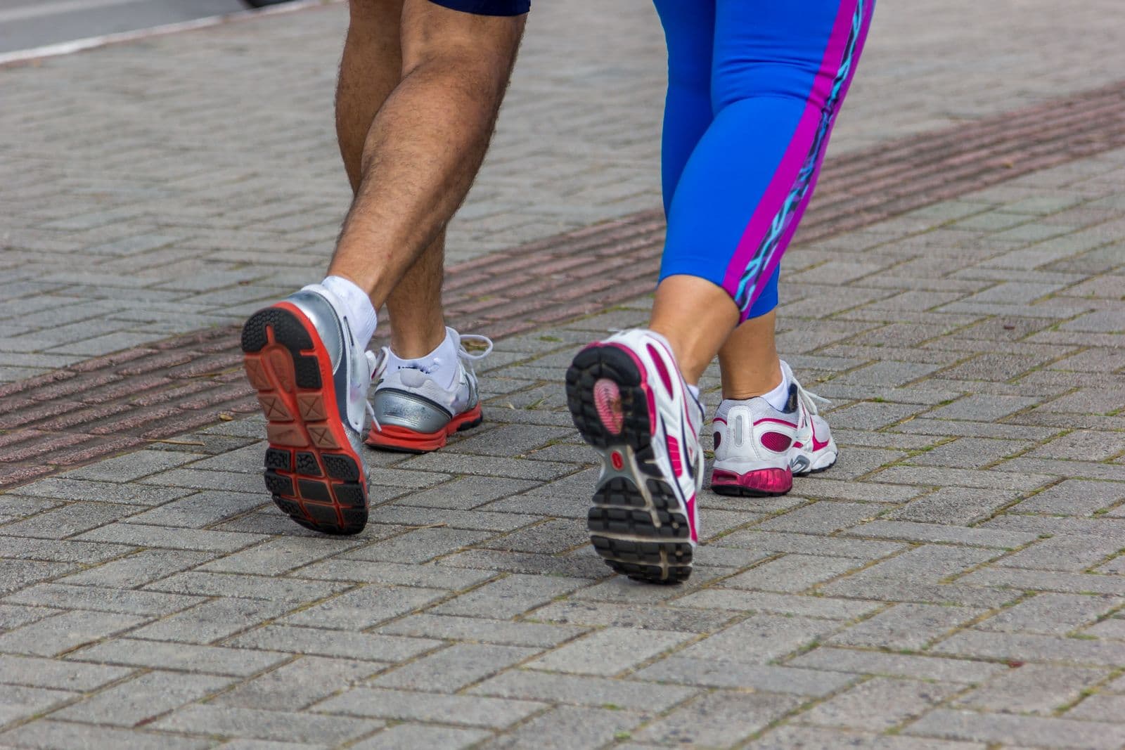 Close-up of two runners' shoes striding on city pavement