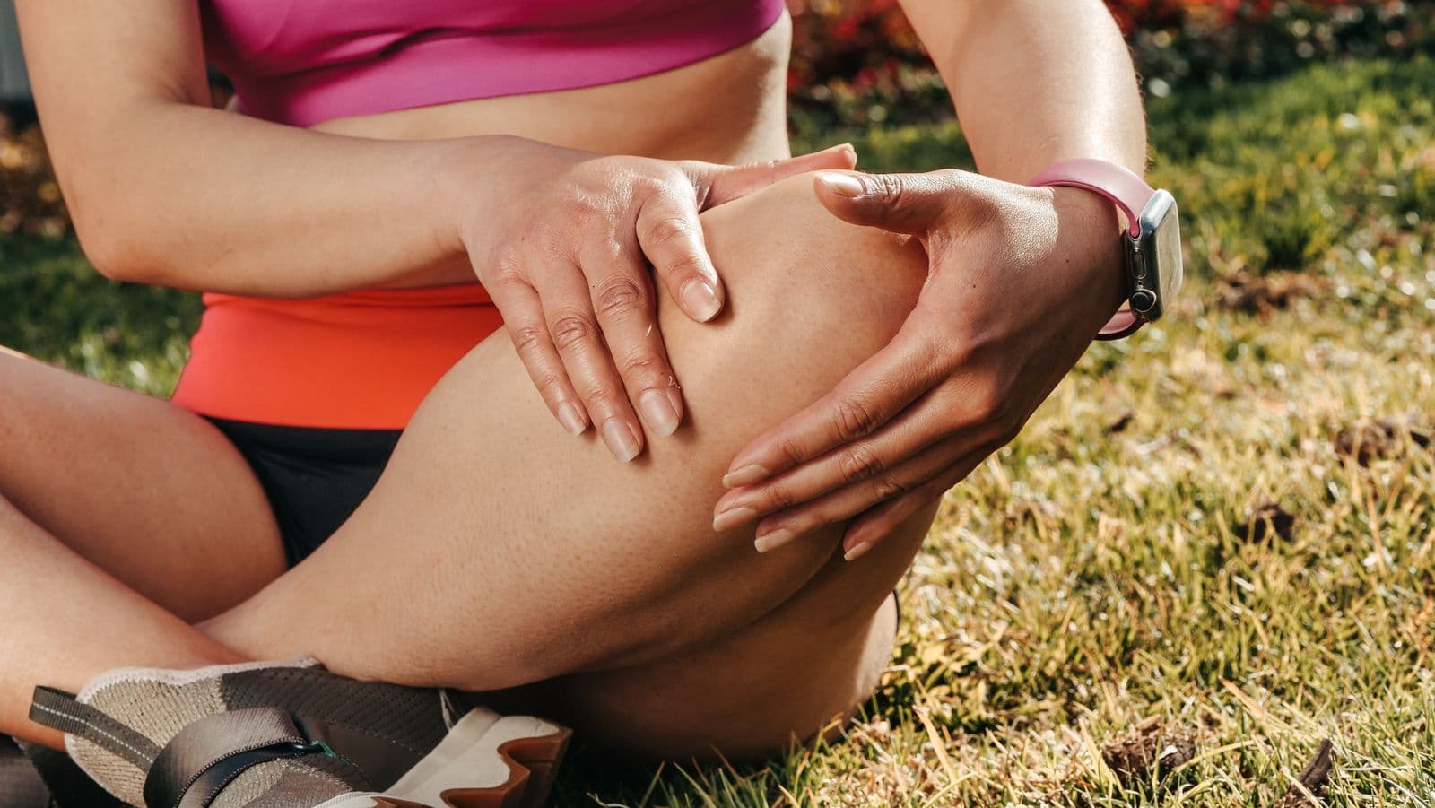 Runner with a sports watch sitting on the grass holding her knee