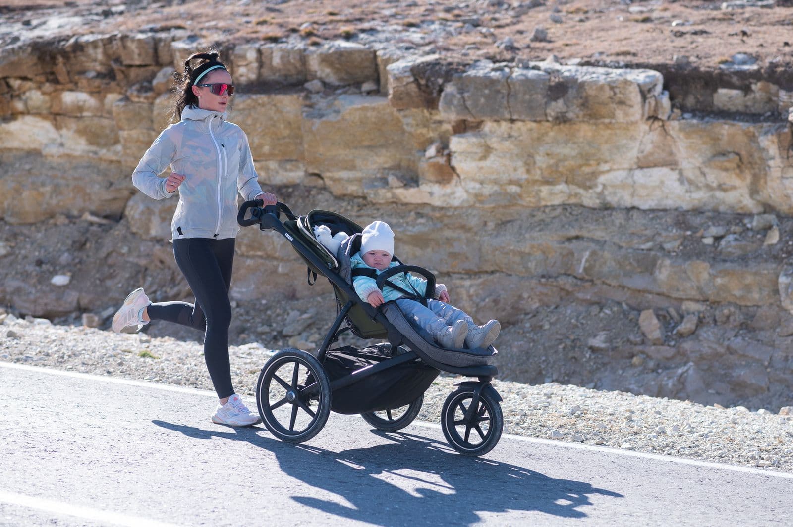 Parent running with a jogging stroller on a sunny path