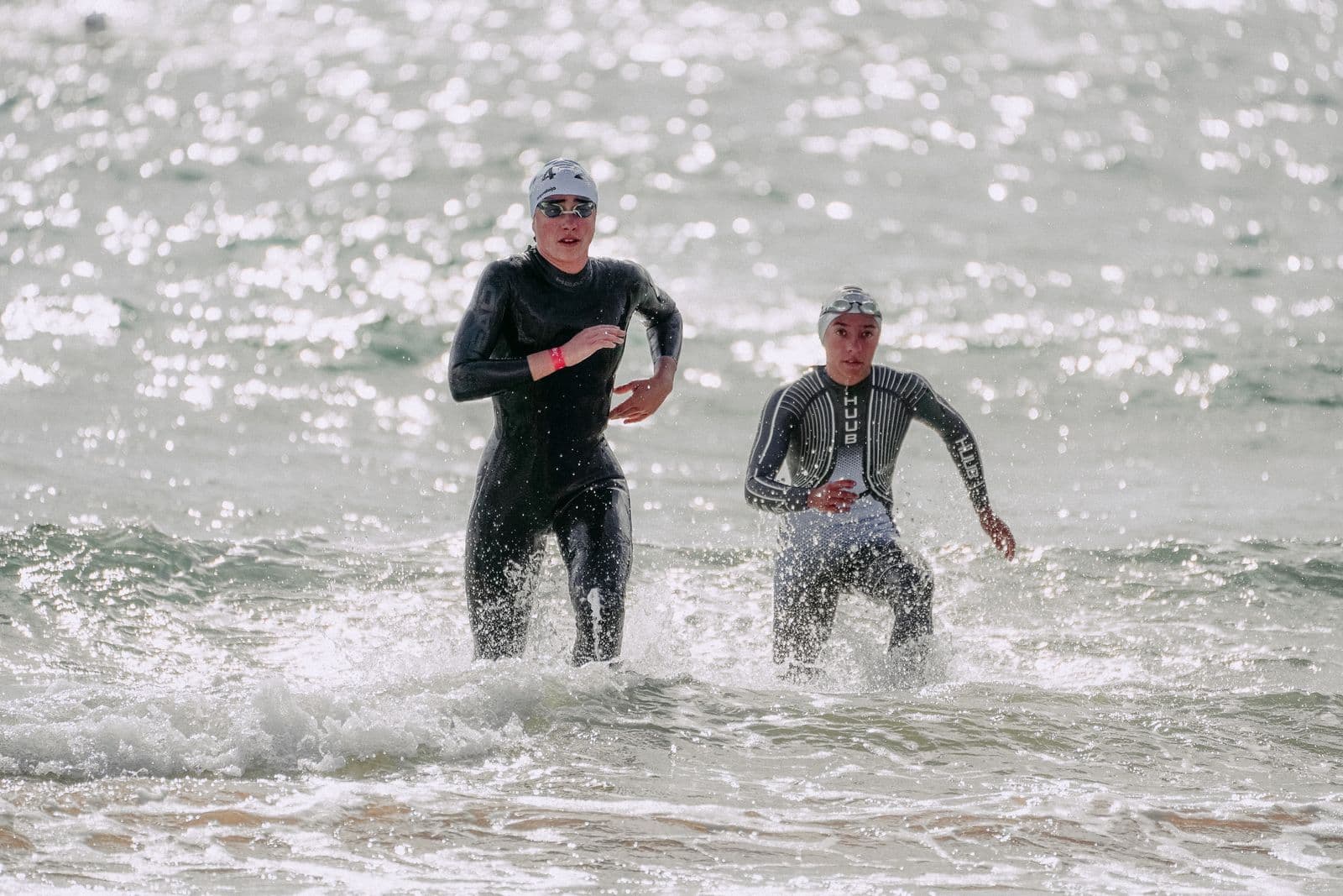 Triathletes in wetsuits running out of the ocean after the swim leg