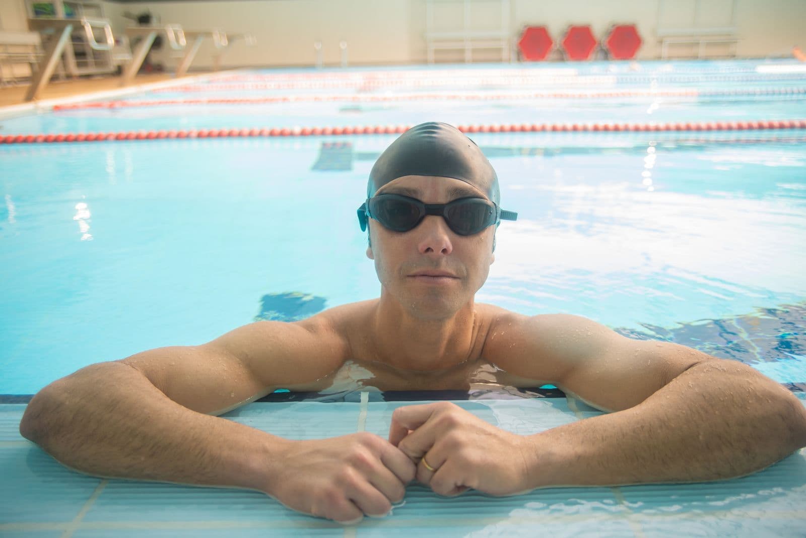 Adult swimmer with goggles resting at the edge of an indoor pool