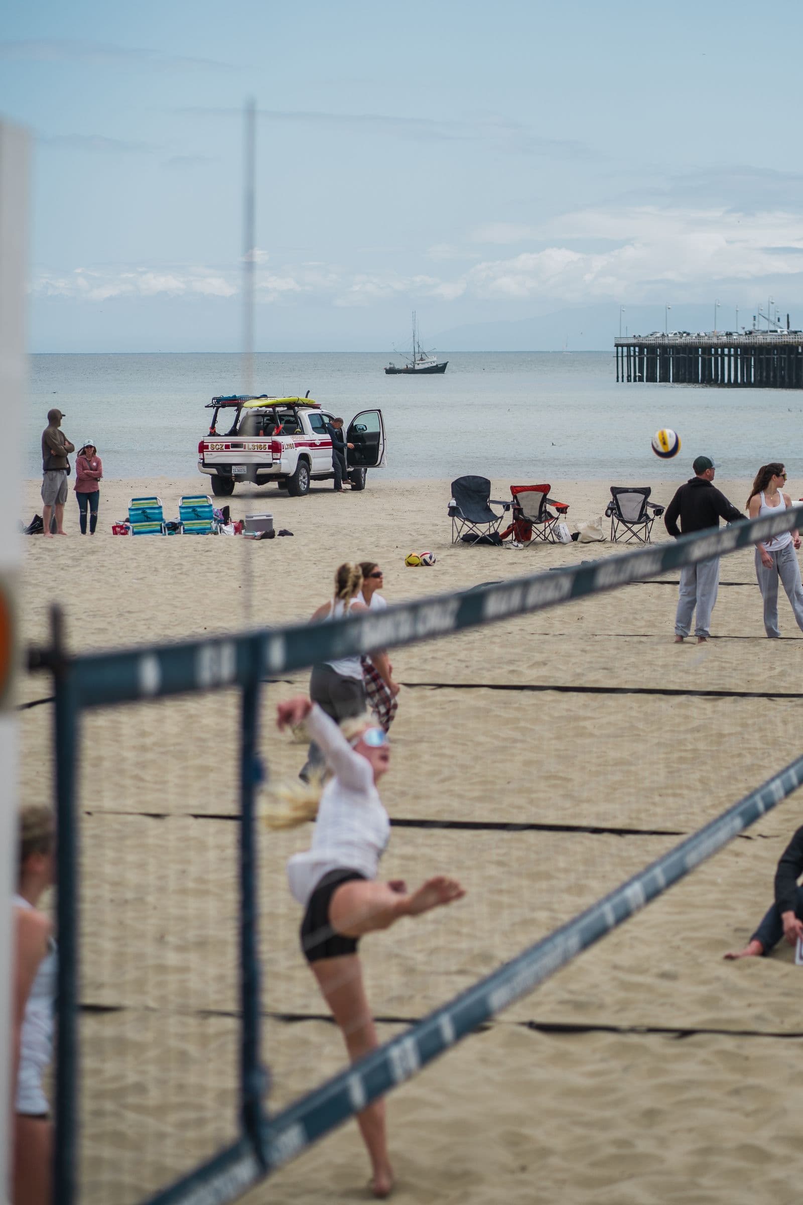 Beach volleyball match beside a pier on the coast